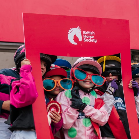 Children in jockey silks with large comedy coloured sunglasses, smiling and posing with a BHS card photo frame