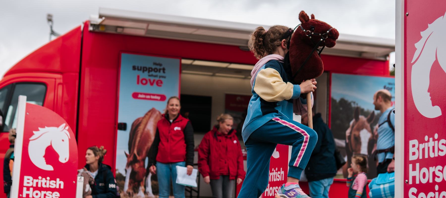 Young girl riding a hobby horse jumping a fence at a stand at a BHS event