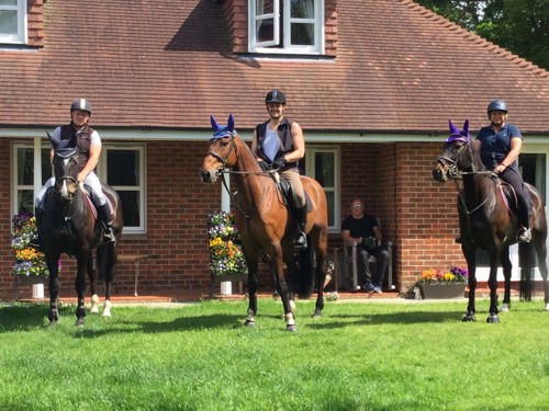 Three horses with riders in front of a house