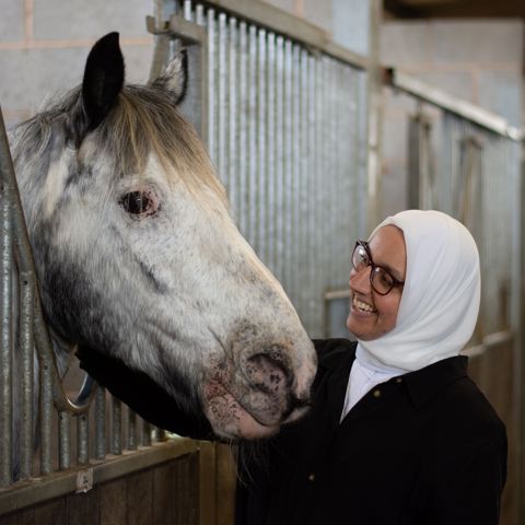 woman smiling at a horse in stables